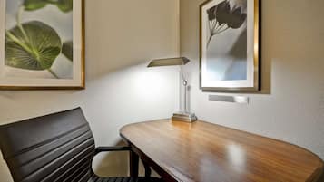 Une chambre d’hôtel avec un bureau en bois, une chaise, une lampe et deux reproductions botaniques encadrées accrochées au mur.