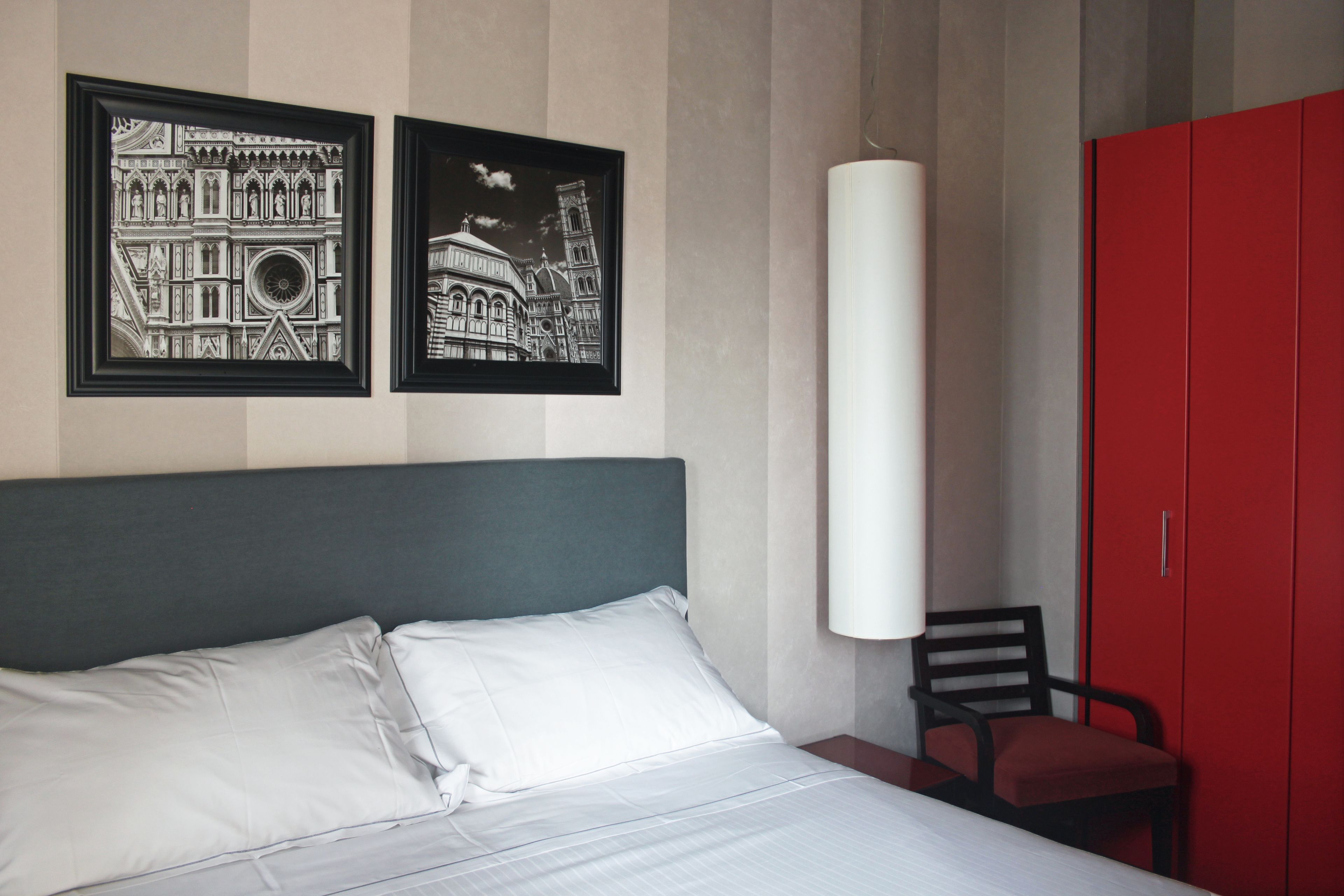 Una habitación de hotel con una cama, dos cuadros enmarcados, un armario rojo y una silla.