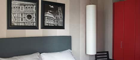 Una habitación de hotel con una cama, dos cuadros enmarcados, un armario rojo y una silla.
