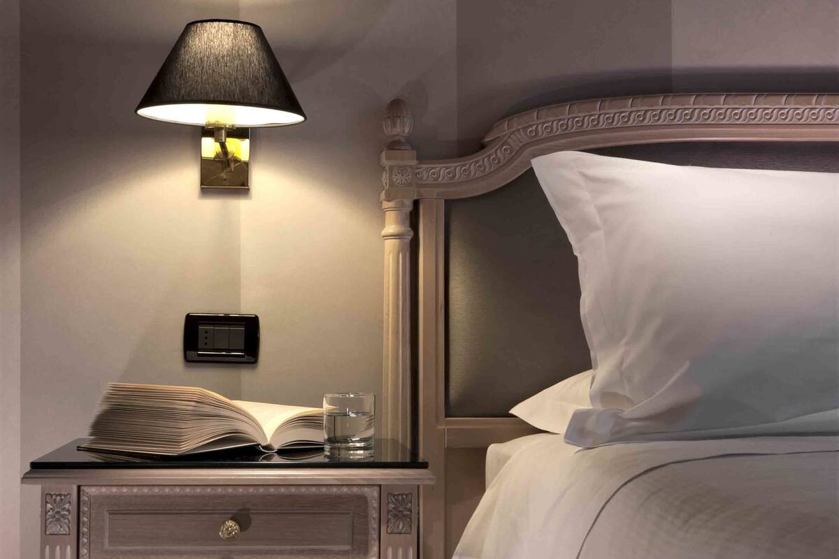A neatly made bed with white linens, a bedside table with a lamp, and a book and glass on the table.