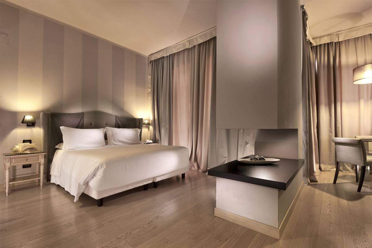 A modern hotel room with a large bed, bedside lamps, a small desk, and a dining area.