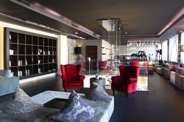 Un área de descanso moderna con una amplia estantería, sillones rojos y una mesa de centro de cristal.