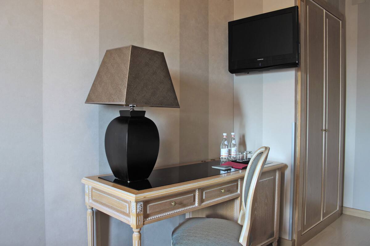 A hotel room with a desk, a lamp, a chair, a television, and a wardrobe.