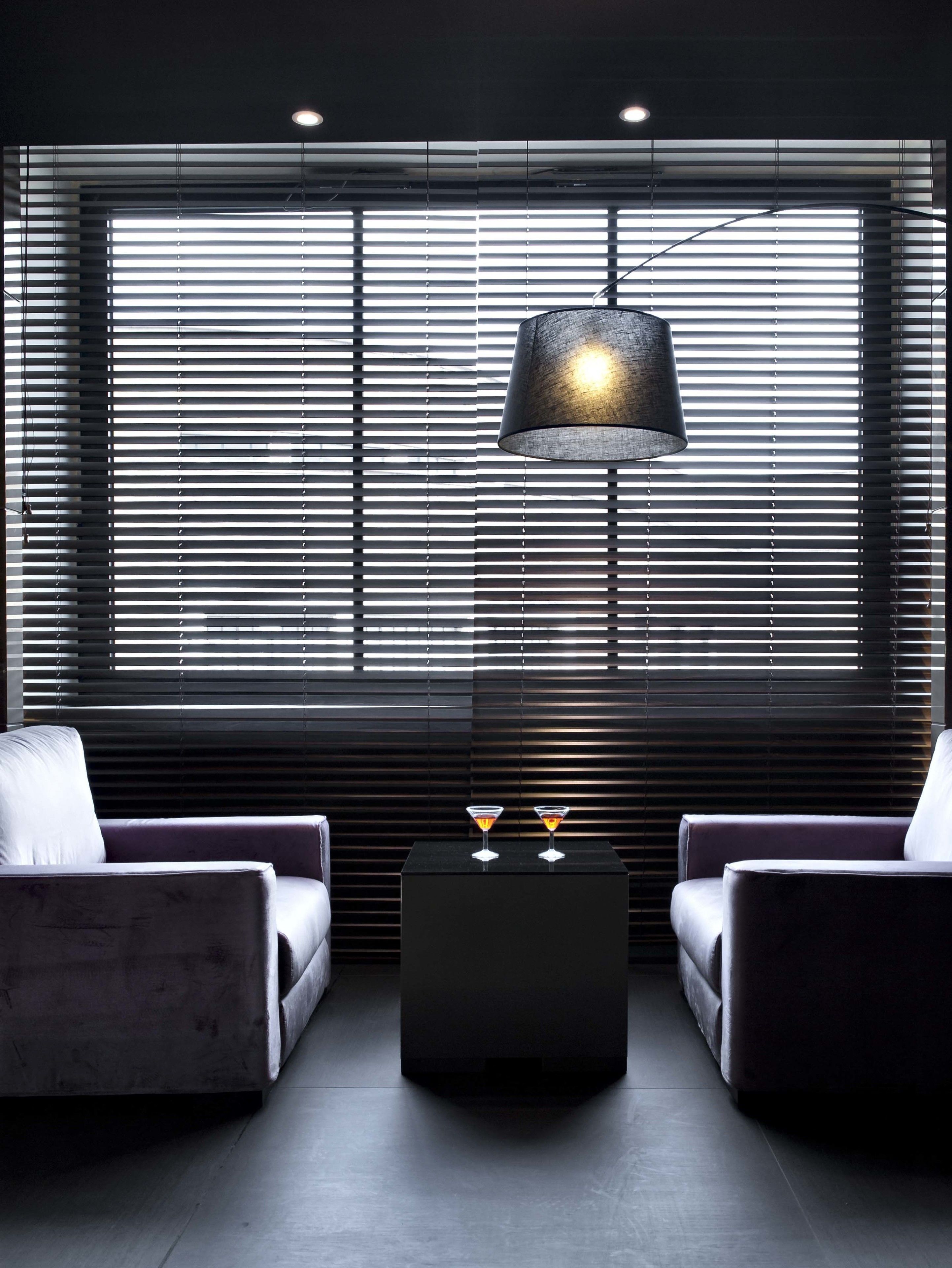 Una habitación moderna con dos sillones, una mesa de centro y un ventanal con persianas horizontales.