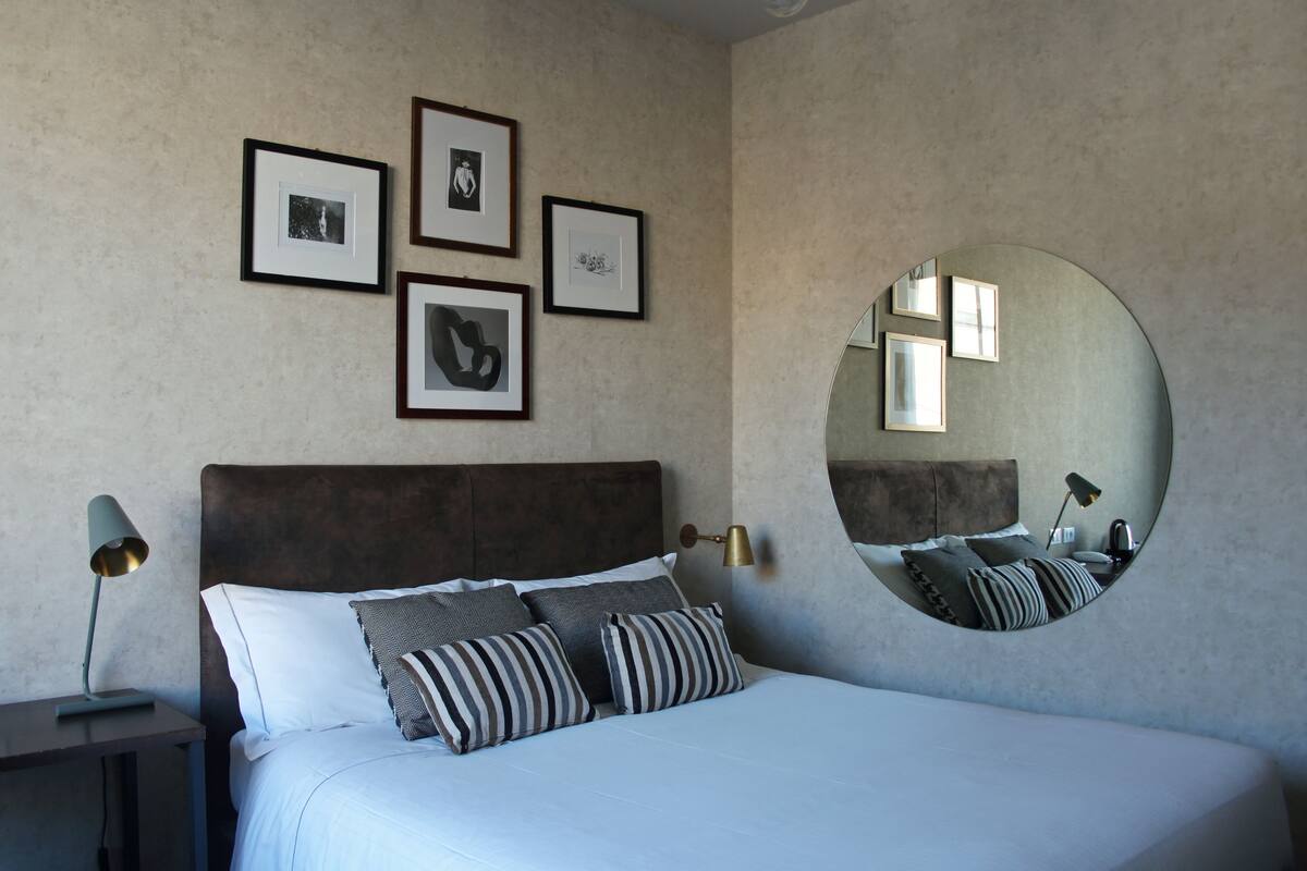 A bedroom with a large bed, a round mirror, framed pictures on the wall, and bedside lamps.
