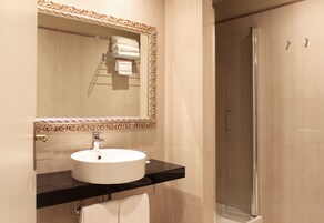 A bathroom with a round sink, a mirror with an ornate frame, and a shower area.