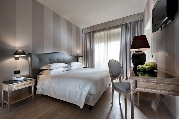 Habitación de hotel con una cama grande, un escritorio con una silla, una lámpara y un televisor en la pared.