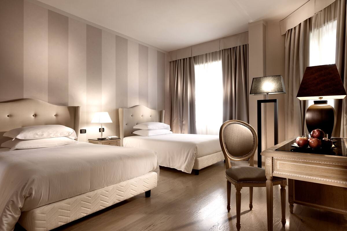 A hotel room with two beds, a desk with a lamp, and a chair.