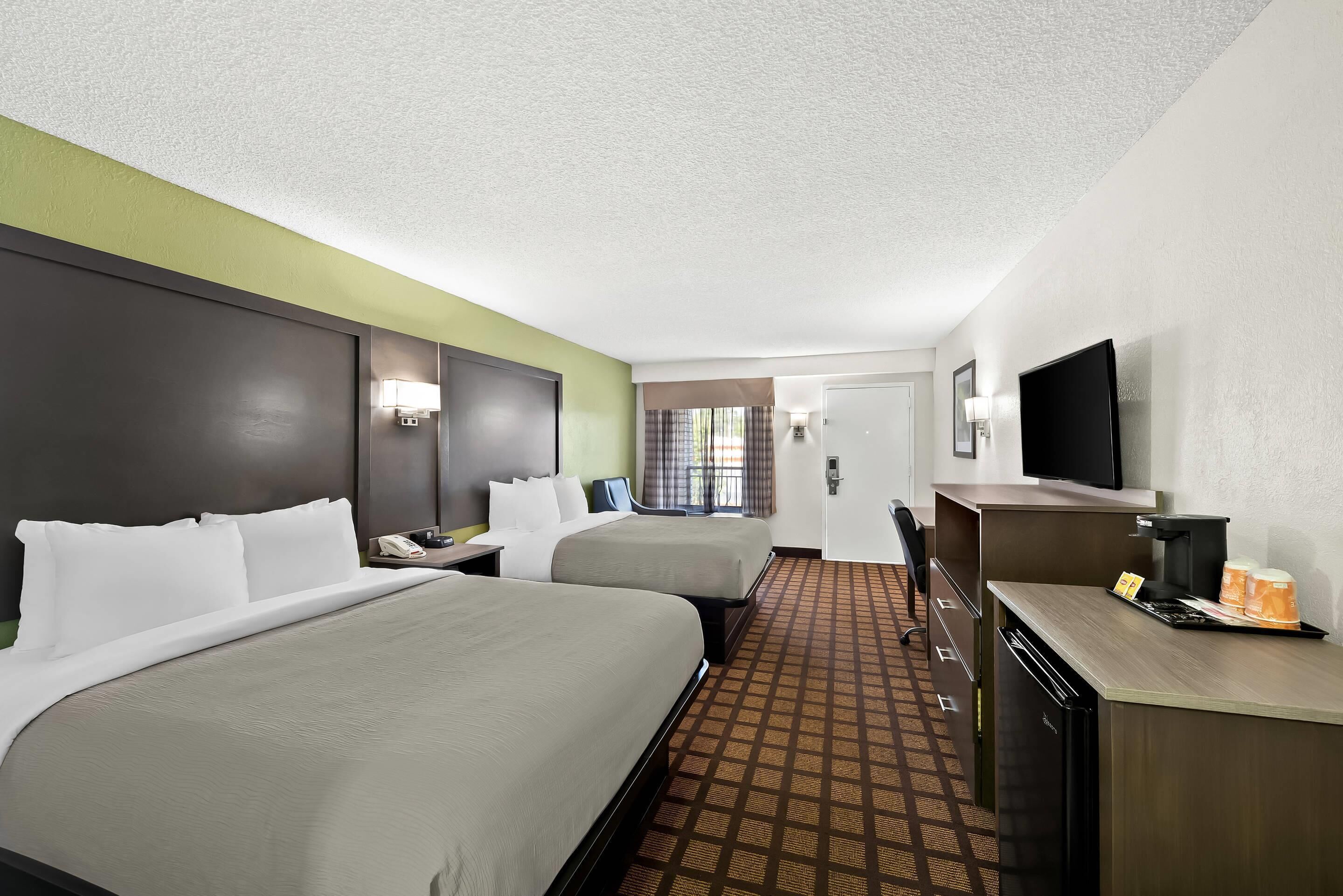 A hotel room with two beds, a desk with a coffee maker, a television, and a bathroom door.
