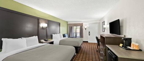A hotel room with two beds, a desk with a coffee maker, a television, and a bathroom door.
