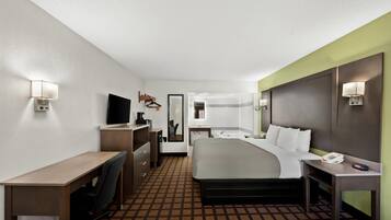 Habitación de hotel con cama, escritorio, silla y baño visible a través de una puerta abierta.