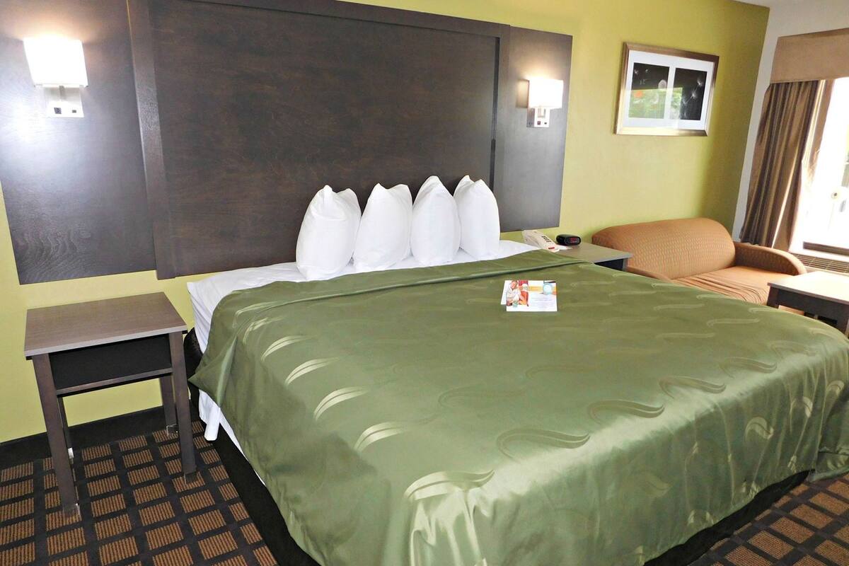 Ein Hotelzimmer mit einem großen Bett, einem Nachttisch, einem Sessel und einem kleinen Tisch mit einer Lampe.