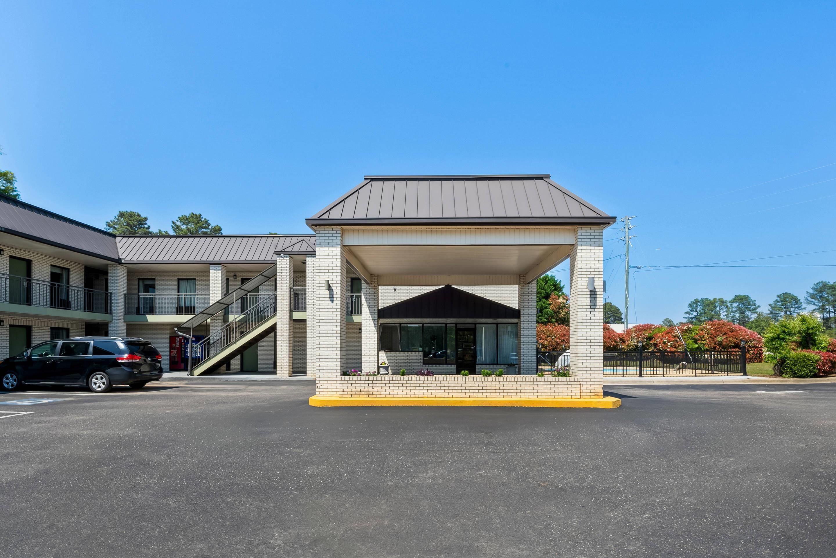 Un motel con un vestíbulo techado, una escalera que lleva al edificio principal y un estacionamiento.