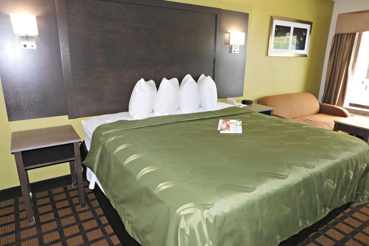 Ein Hotelzimmer mit einem großen Bett, einem Nachttisch, einem Sessel und einem kleinen Tisch.