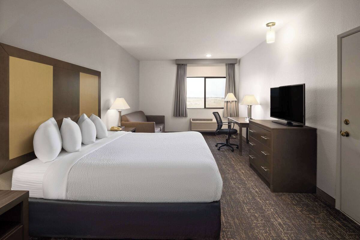 A hotel room with a large bed, a desk, a television, and a window with curtains.