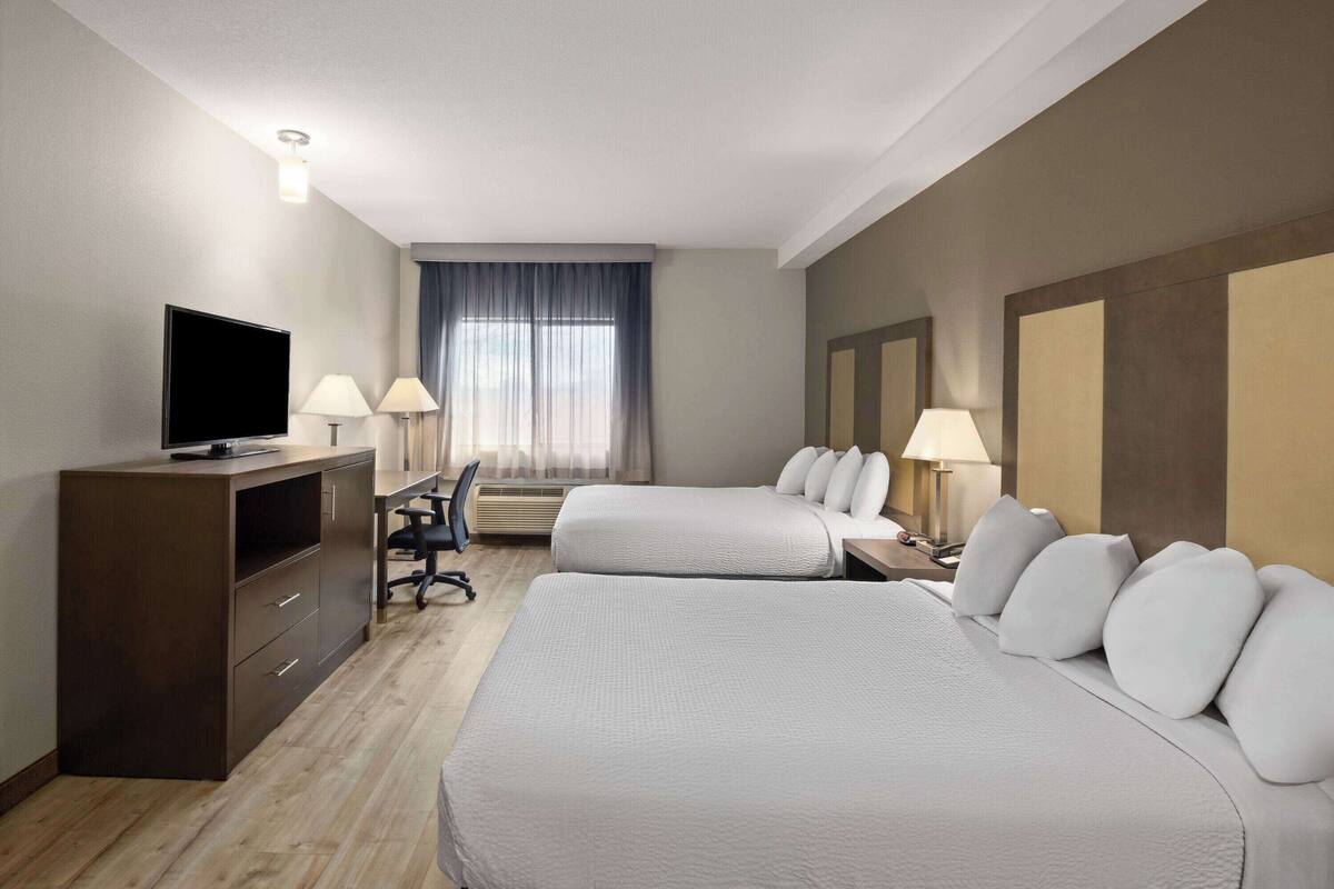 A hotel room with two beds, a desk, a TV, and a window with curtains.