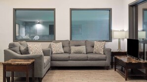 Una sala de estar con un sofá gris, dos sillones, una mesa de centro, un televisor y una lámpara.
