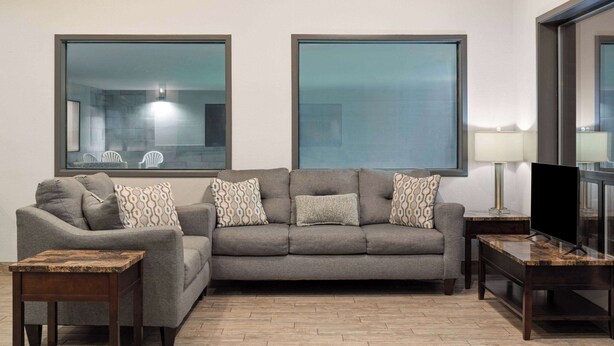 Una sala de estar con un sofá gris, dos sillones, una mesa de centro, un televisor y una lámpara.