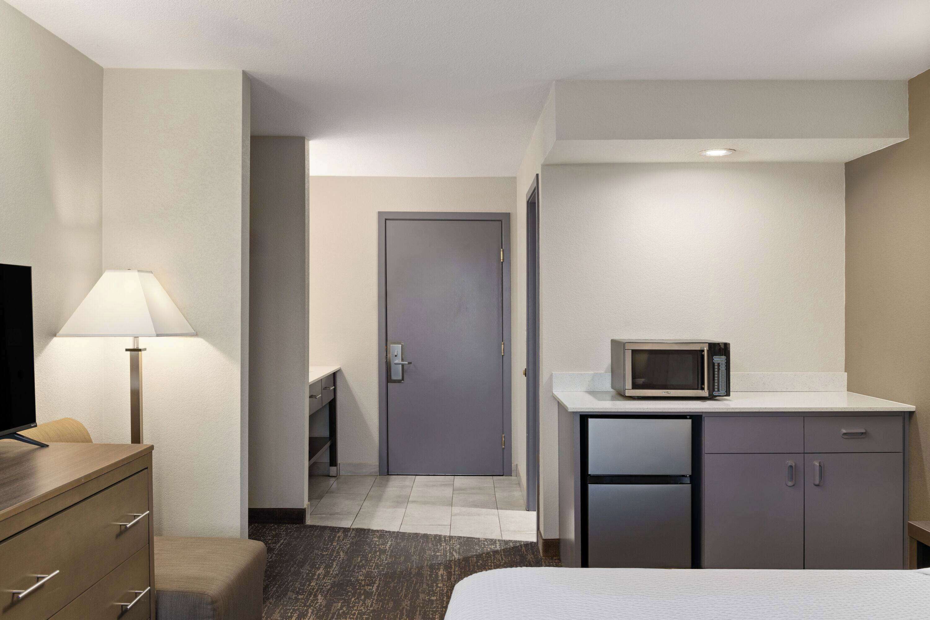Ein Hotelzimmer mit Bett, Schreibtisch mit Lampe, Mikrowelle und Kühlschrank.