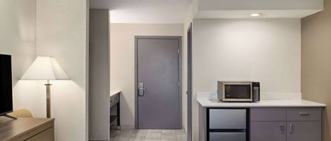 Ein Hotelzimmer mit Bett, Schreibtisch mit Lampe, Mikrowelle und Kühlschrank.