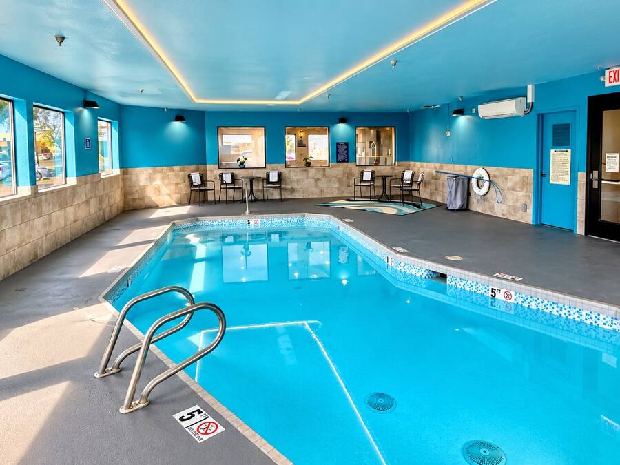 Una piscina interior con carriles delimitados, una silla de salvavidas y una zona junto a la piscina con sillas y mesas.