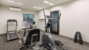 A fitness room with a treadmill, elliptical, and dumbbells.