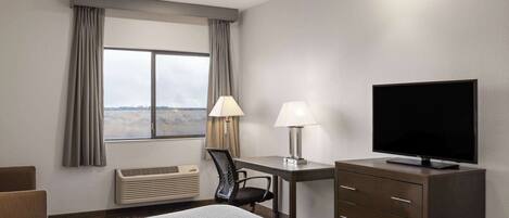 A hotel room with a bed, desk, chair, television, and a window with curtains.