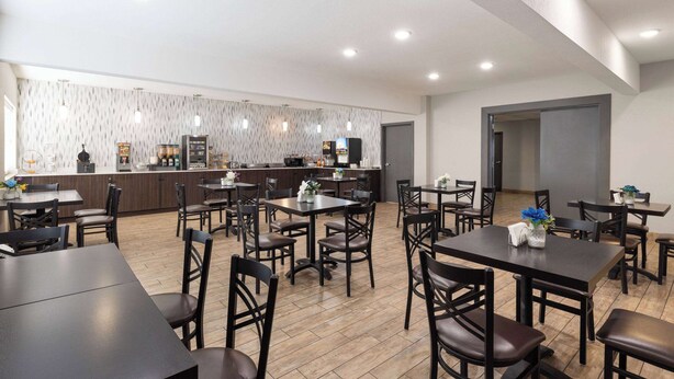 Un comedor moderno con varias mesas y sillas, una barra con estación de bebidas y una pared con diseño.