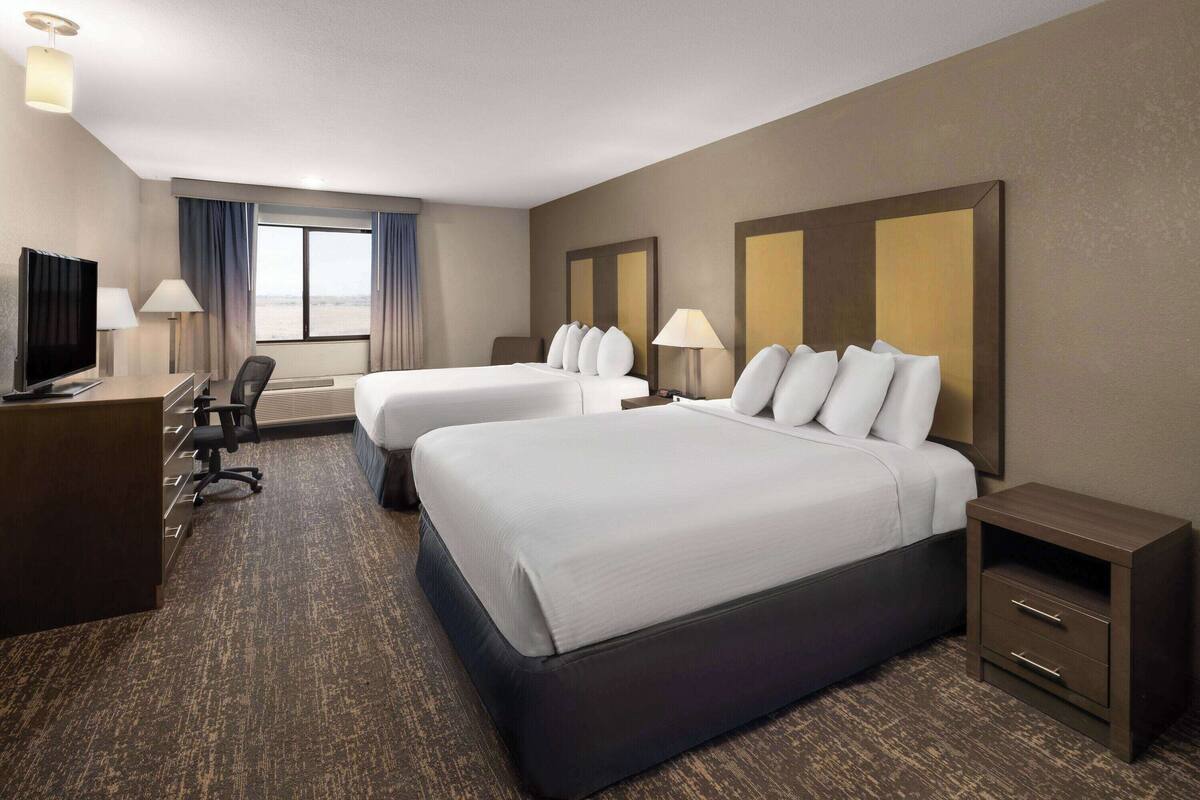 A hotel room with two beds, a desk, a TV, and a view of the outdoors.