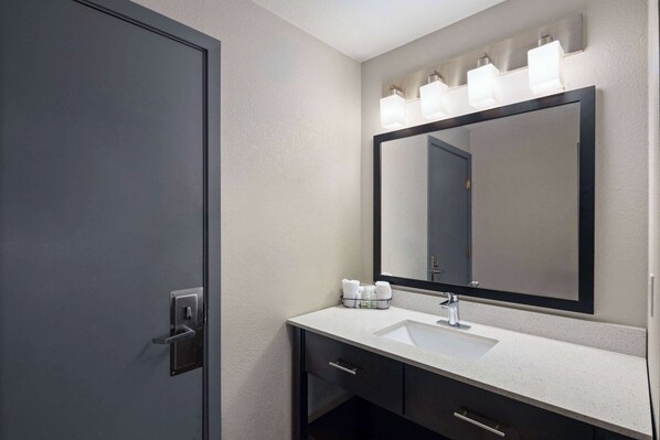 A modern bathroom with a dark door, a white sink, a large mirror, and a lighted vanity area.