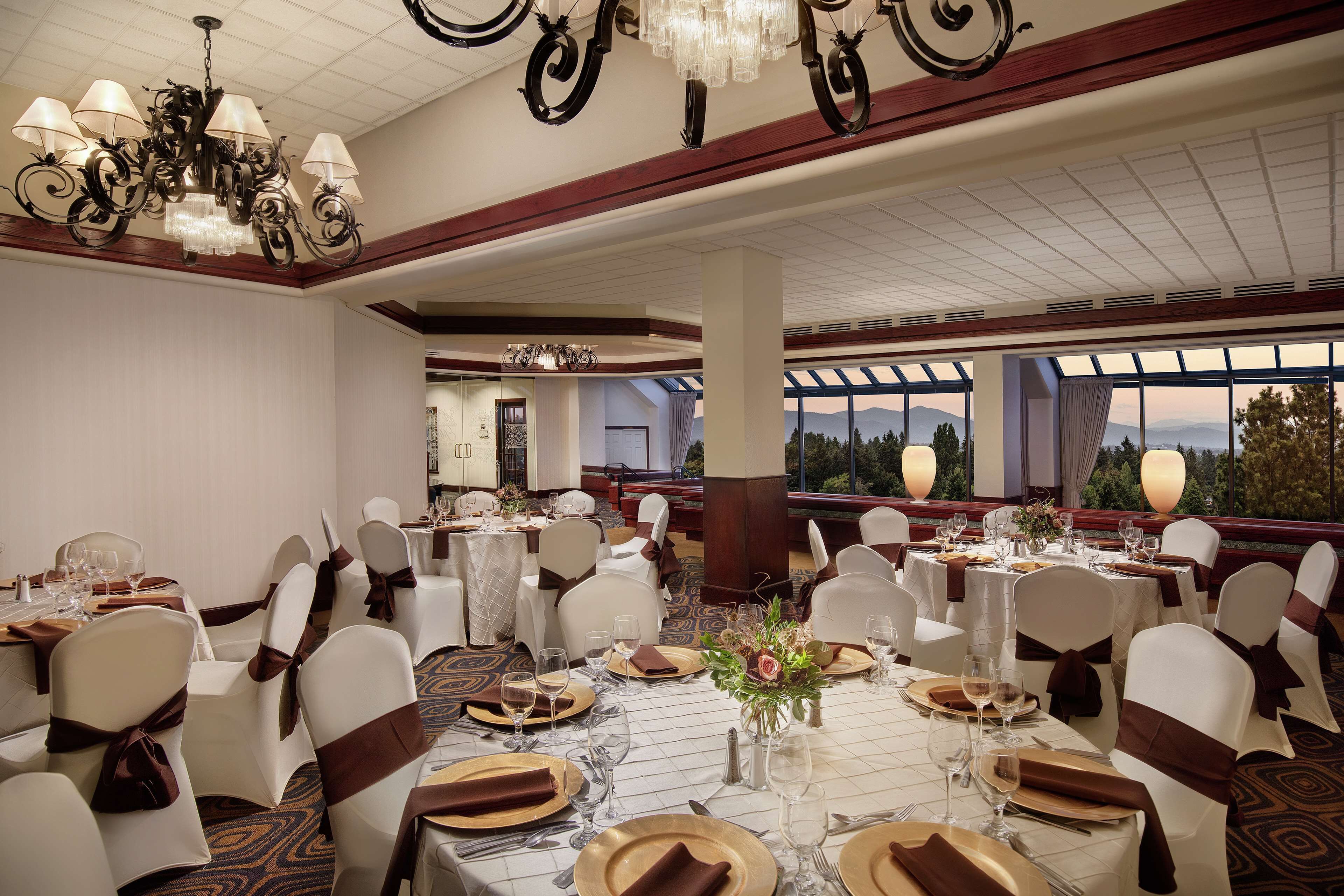 A banquet hall with round tables, white chairs, and chandeliers.
