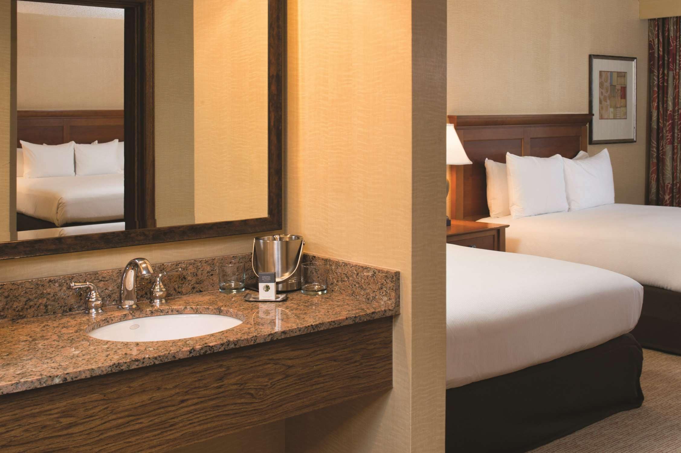 A hotel room with a granite countertop sink, a mirror, a bed with white linens, and a wooden headboard.