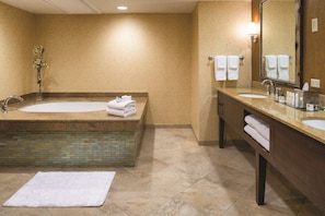 A bathroom with a large bathtub, two sinks, a mirror, and a towel rack.