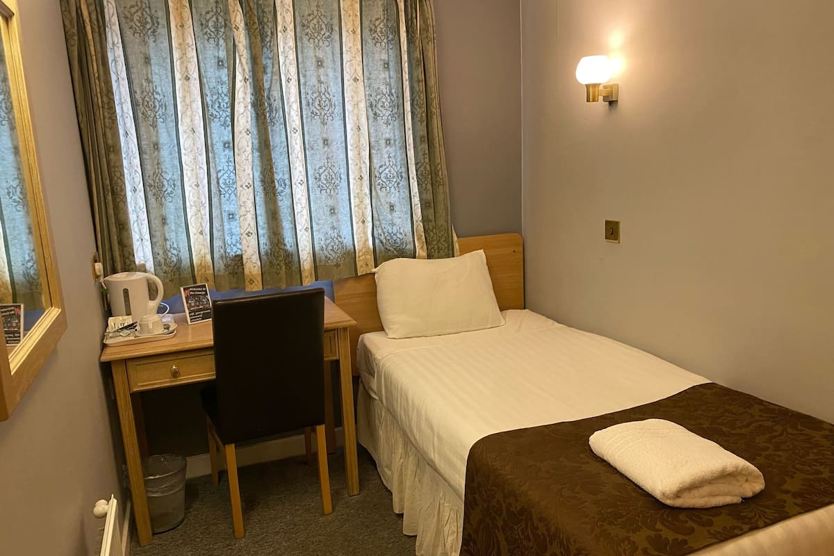 A hotel room with a bed, a desk with a chair, a coffee maker, and a sign.