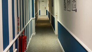 A hallway with blue and white striped walls, a fire extinguisher, and a door at the end. - The George Hotel (Reading)