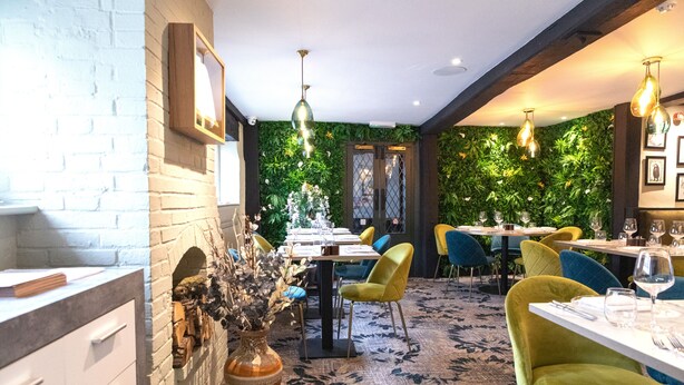 A restaurant with brick walls, green walls with plants, and yellow chairs. - The George Hotel (Reading)