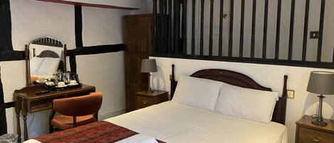 A hotel room with a large bed, a desk with a chair, a dresser, a mirror, and a nightstand with a lamp.