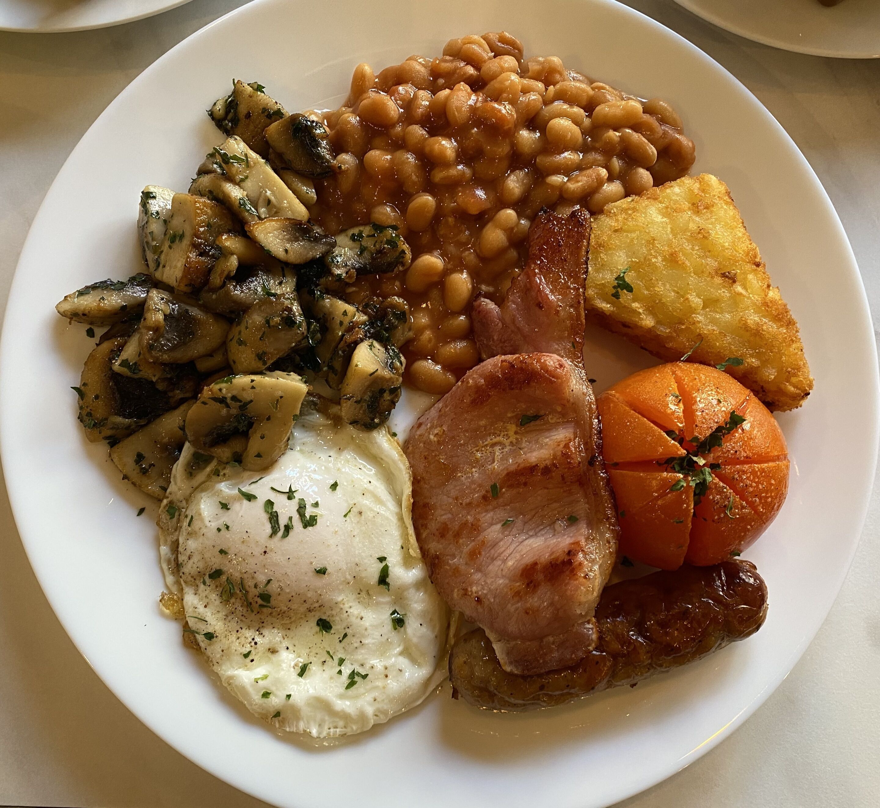 A plate of food including beans, bacon, eggs, mushrooms, and a baked potato.