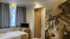 A hotel room with two beds, a television on a wooden nightstand, a door leading to another room, and a large floral mural on the wall. - The George Hotel (Reading)
