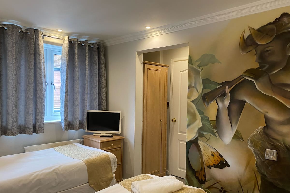A hotel room with two beds, a television on a wooden nightstand, a door leading to another room, and a large floral mural on the wall.