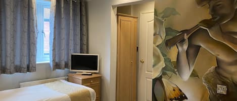 A hotel room with two beds, a television on a wooden nightstand, a door leading to another room, and a large floral mural on the wall.