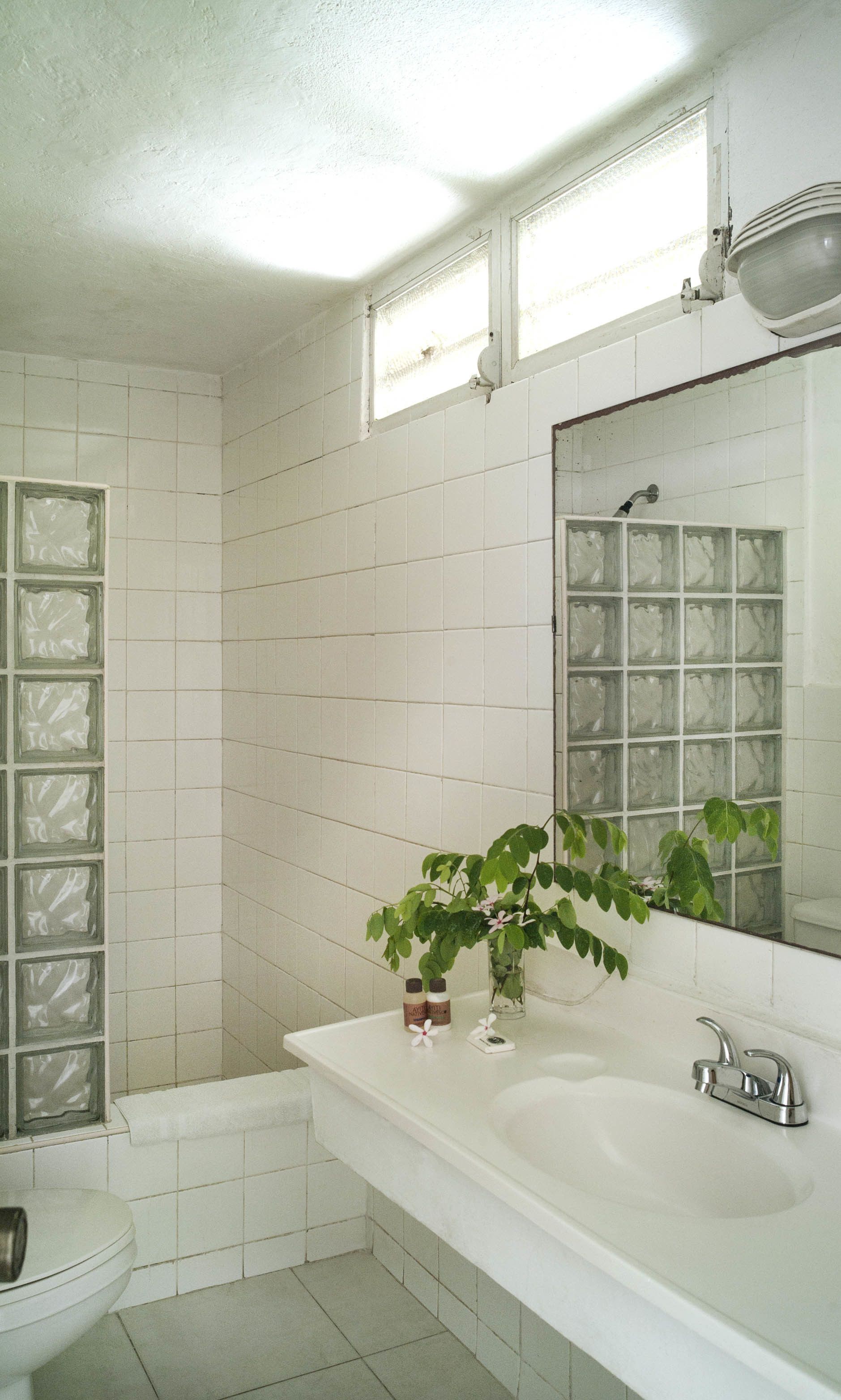 Ein Badezimmer mit weißen Fliesen, einem Waschbecken, einem Spiegel und einer Dusche.