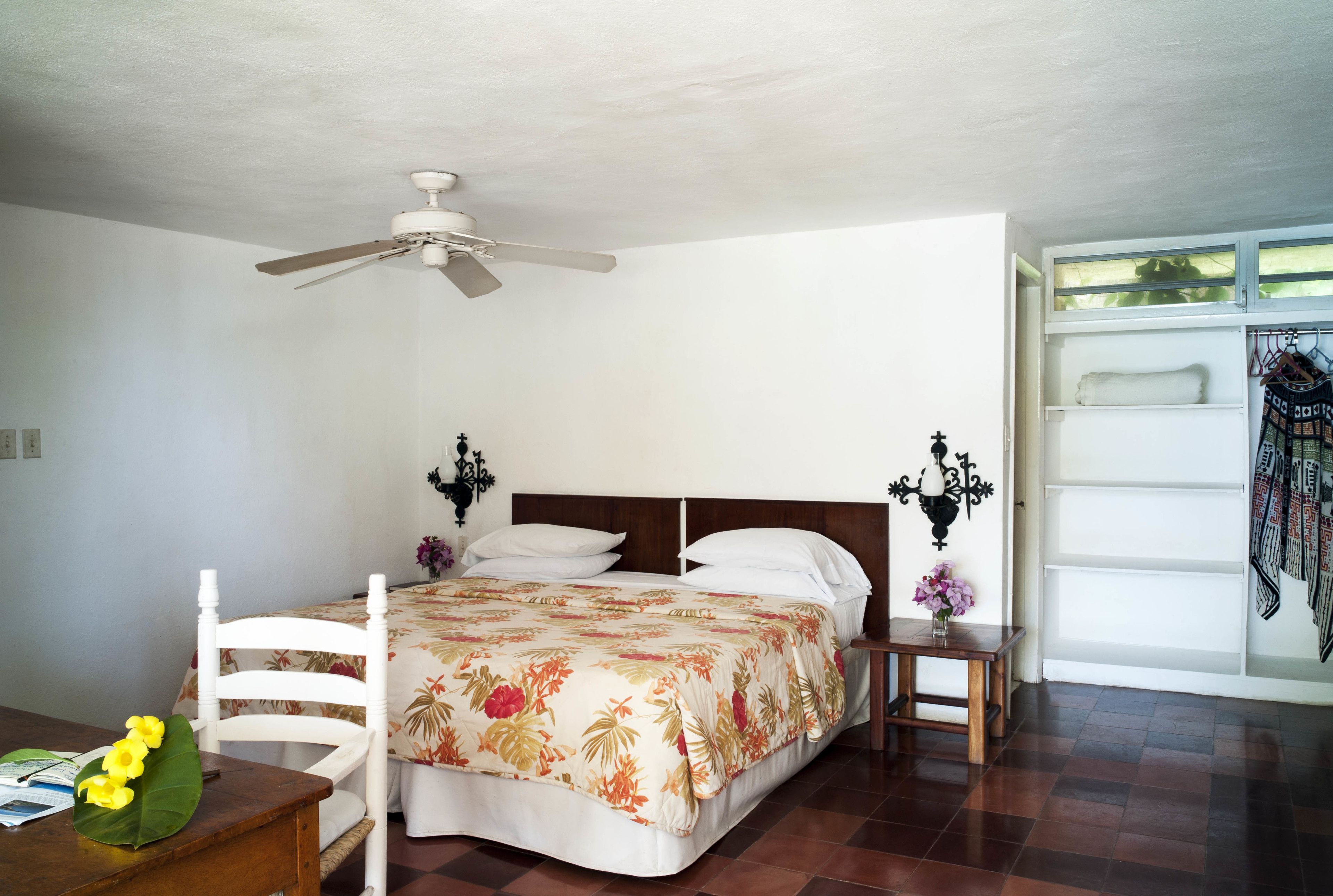 A bedroom with a bed, a ceiling fan, a nightstand, a chair, and a window with a view.