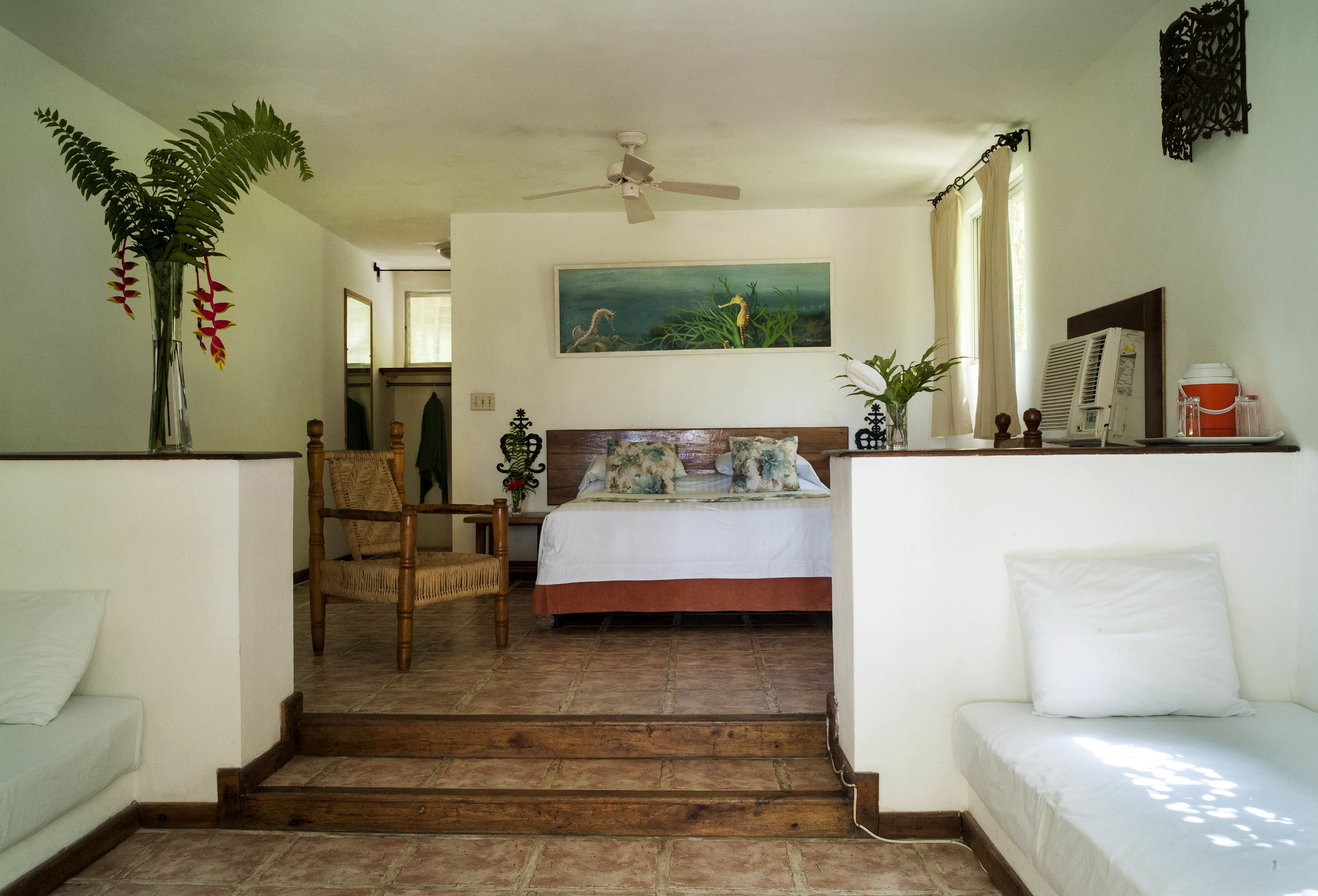 A bedroom with a bed, a chair, a staircase, a ceiling fan, and a painting on the wall.