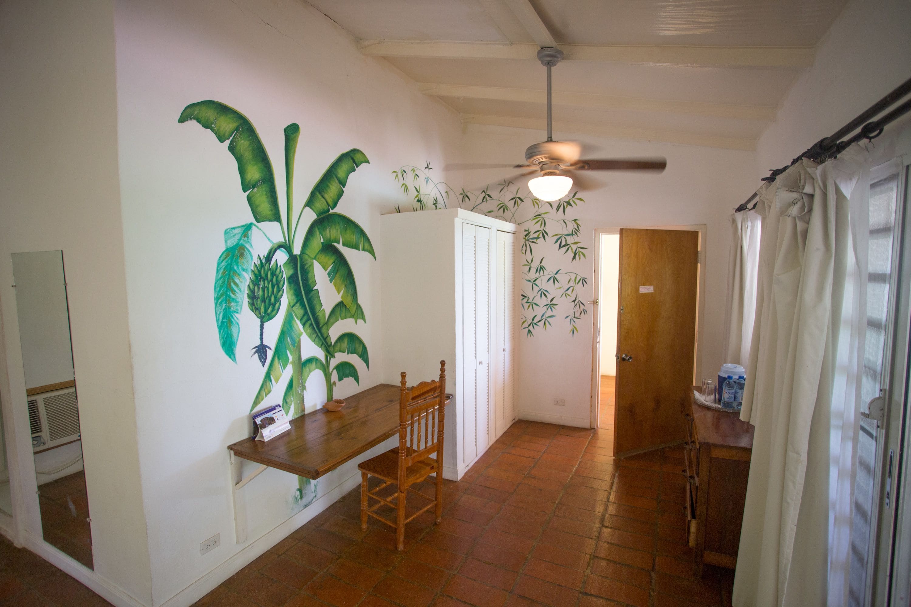 Ein Flur mit Deckenventilator, einer Holzbank, einem Stuhl und einer Wand mit großem Pflanzenwandbild.
