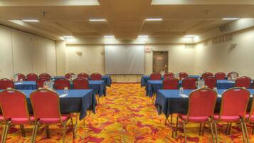 Une salle de conférence avec des rangées de tables et de chaises, un sol recouvert de moquette et un écran de projection.