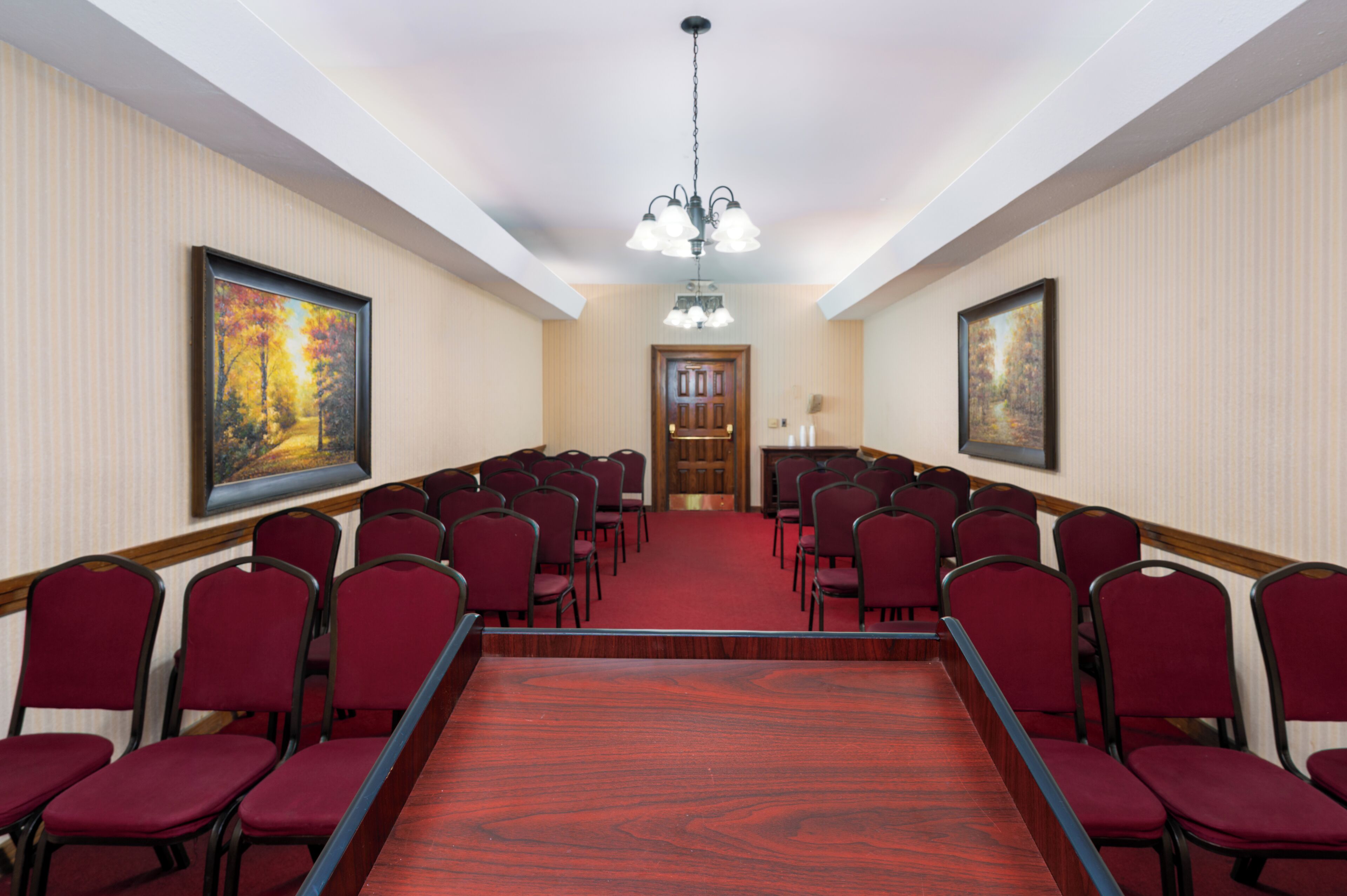 A conference room with rows of red chairs, a wooden conference table, and two large paintings on the walls.