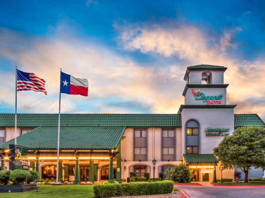 Un hotel con techo verde, una torre de campanas y banderas de Estados Unidos y Texas.