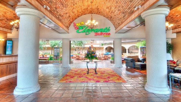 En lobby med flisegulv, en central blomsterdekoration og et skilt med teksten "MGM Elegante Suites".