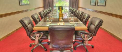 Une salle de conférence avec une longue table, des fauteuils en cuir et une moquette rouge.